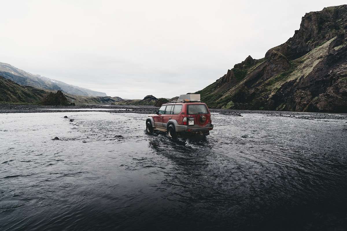An SUV driving through water, near mountains